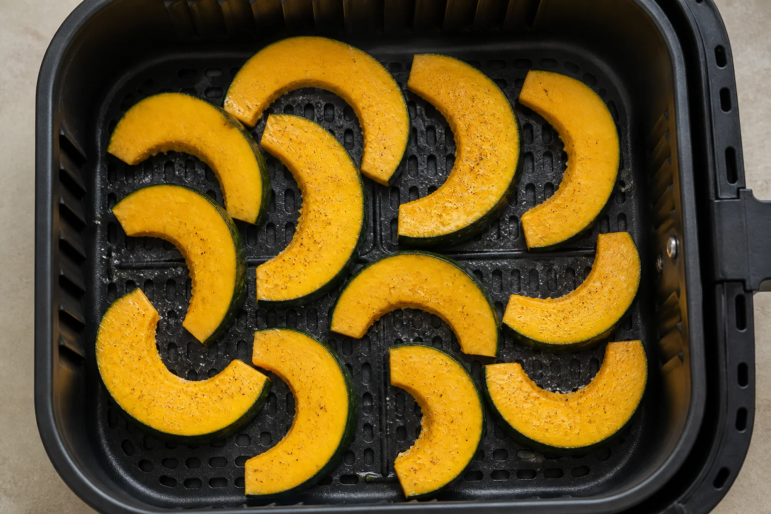 Uncooked acorn squash half-moons arranged in one layer in an air fryer basket