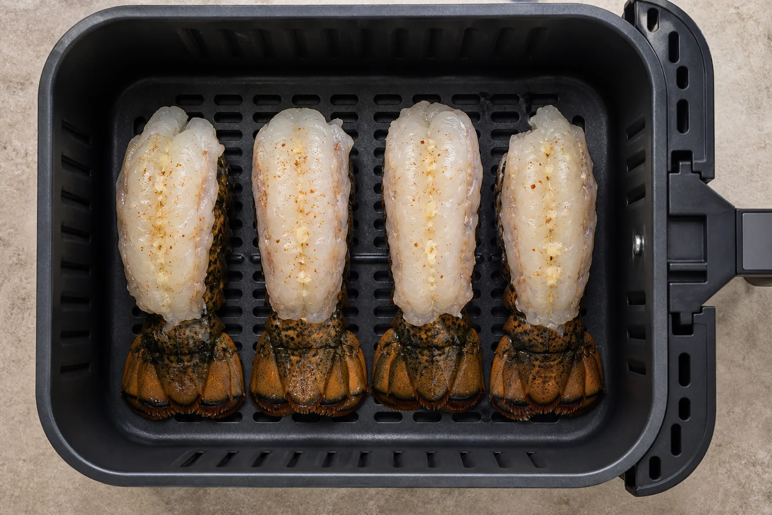 Four raw butterflied lobster tails arranged shell-side down in an air fryer basket