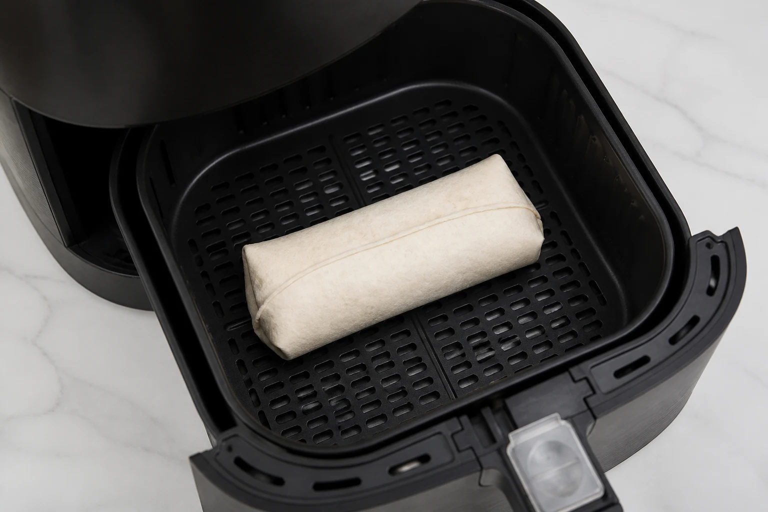 Frozen burrito seam-side up in the center of an air-fryer basket before cooking.