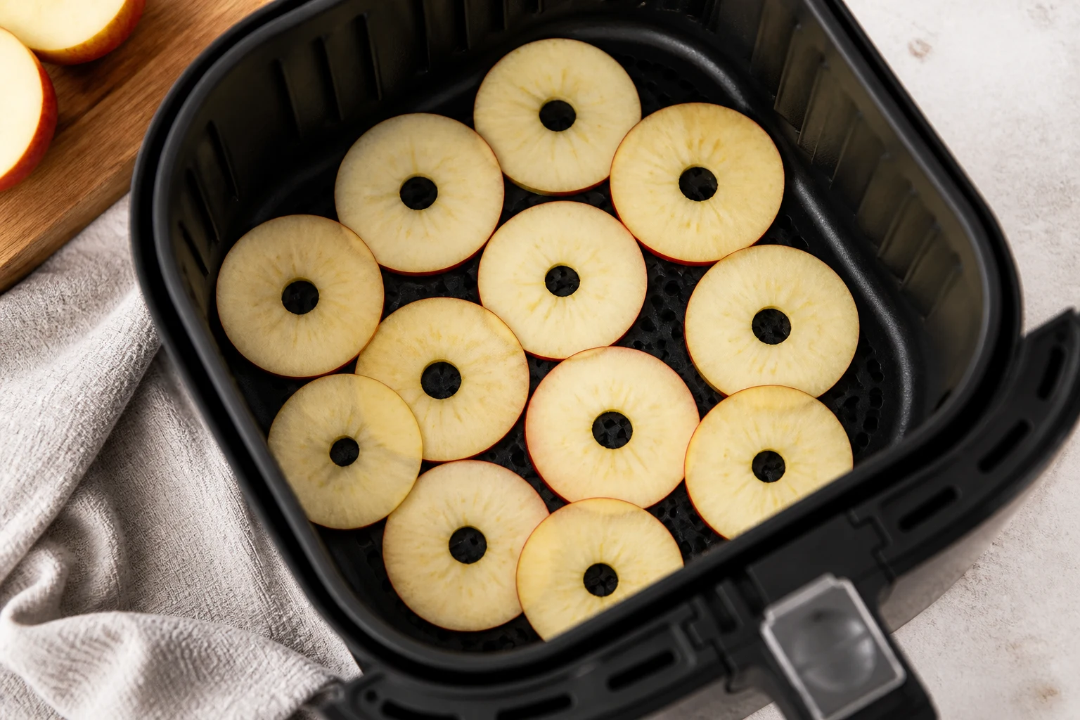 Very thin apple rings arranged in a single layer in an air-fryer basket before drying.
