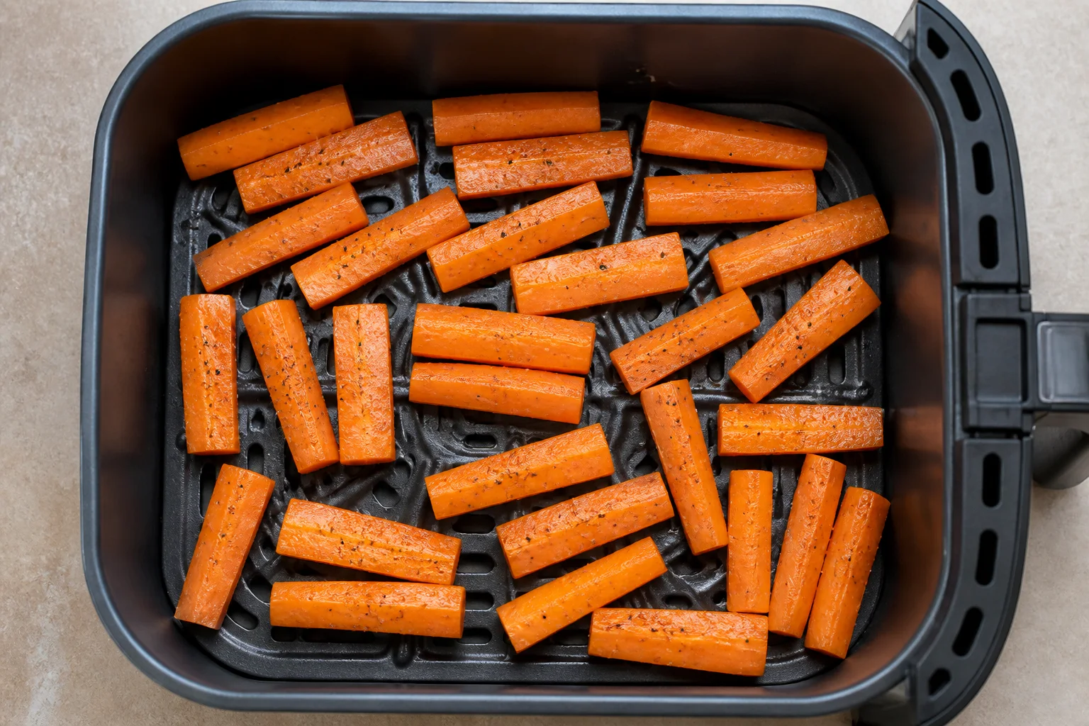 Raw seasoned carrot batons arranged in one layer in an air fryer basket