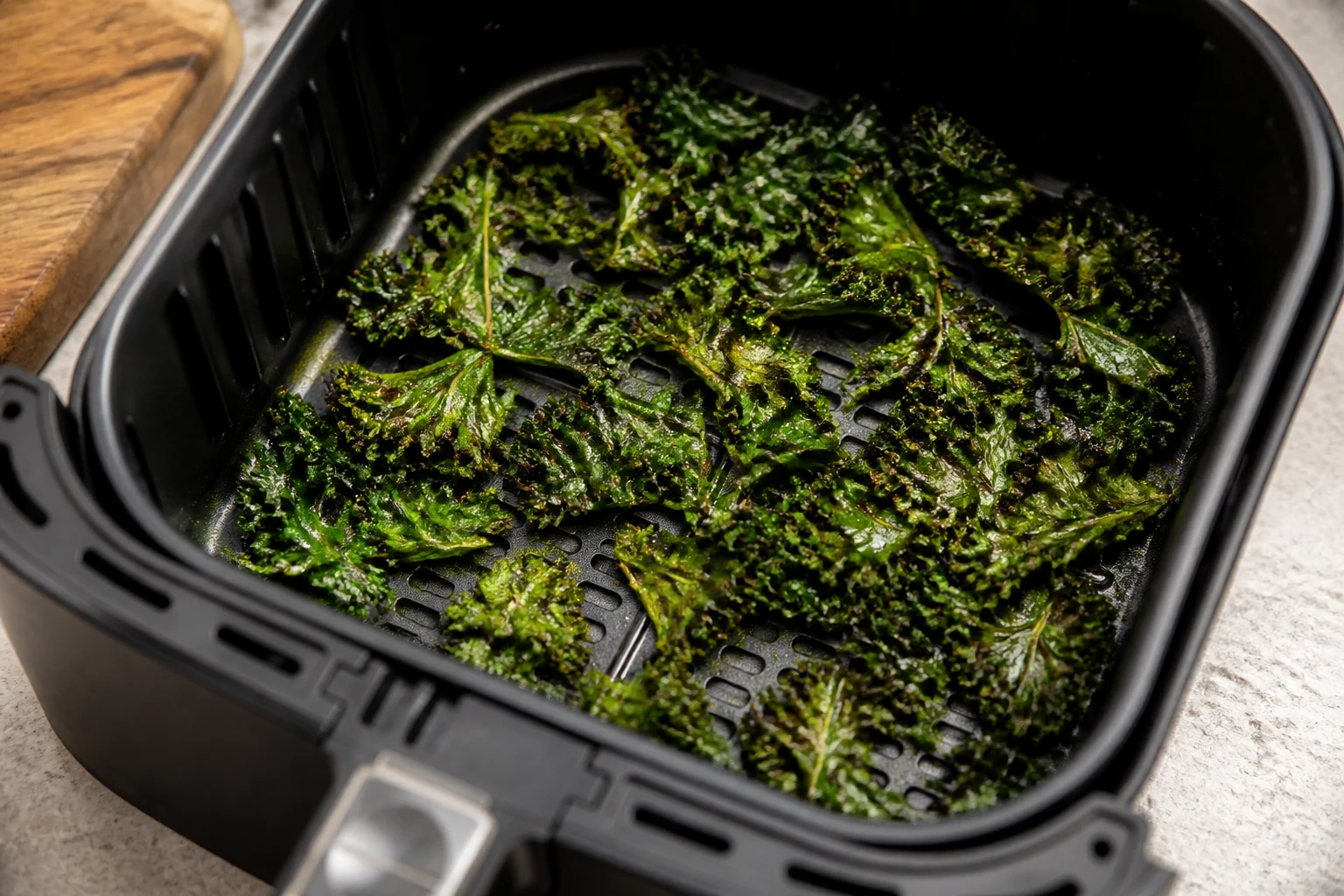 Lightly oiled kale pieces in a loose single layer in an air-fryer basket, edges visibly crisping.