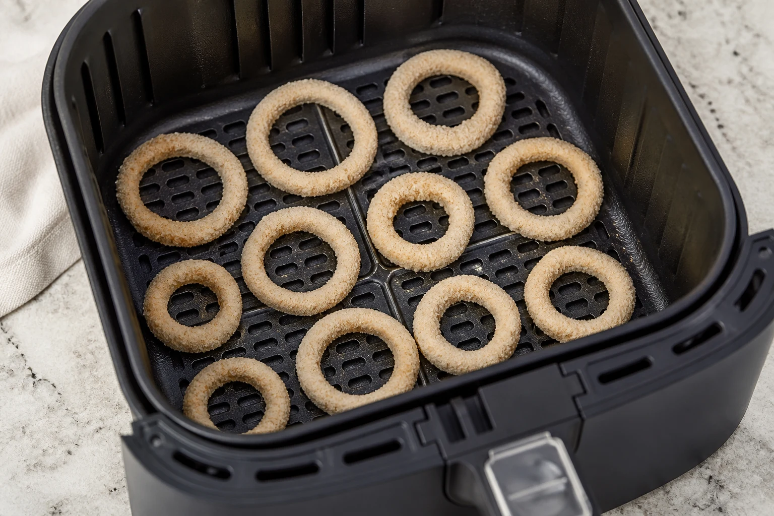 Breaded onion rings spaced in a single layer in an air-fryer basket with a light, even oil mist.