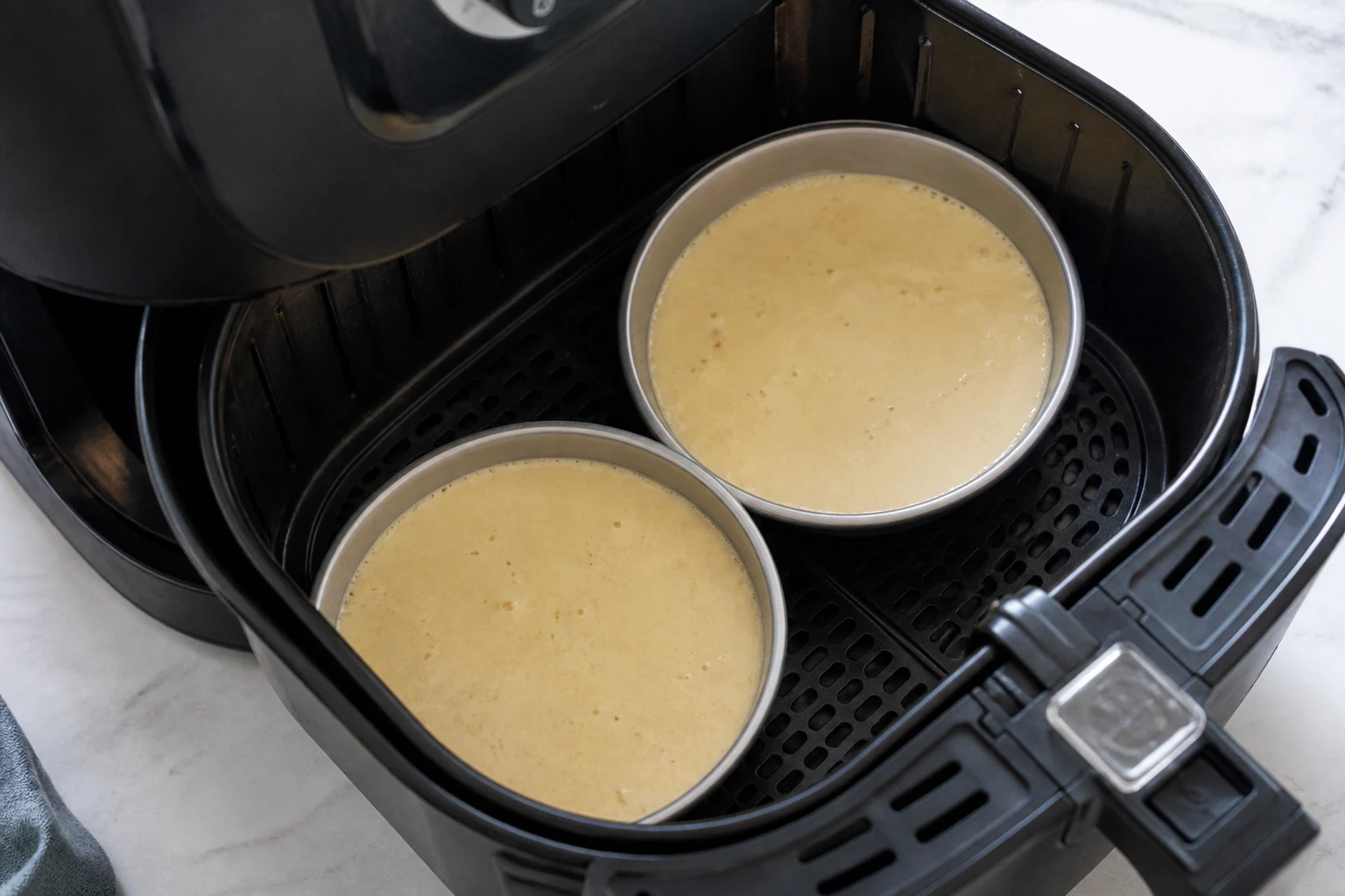 Pancake batter in two shallow greased round pans sitting inside an air-fryer basket.