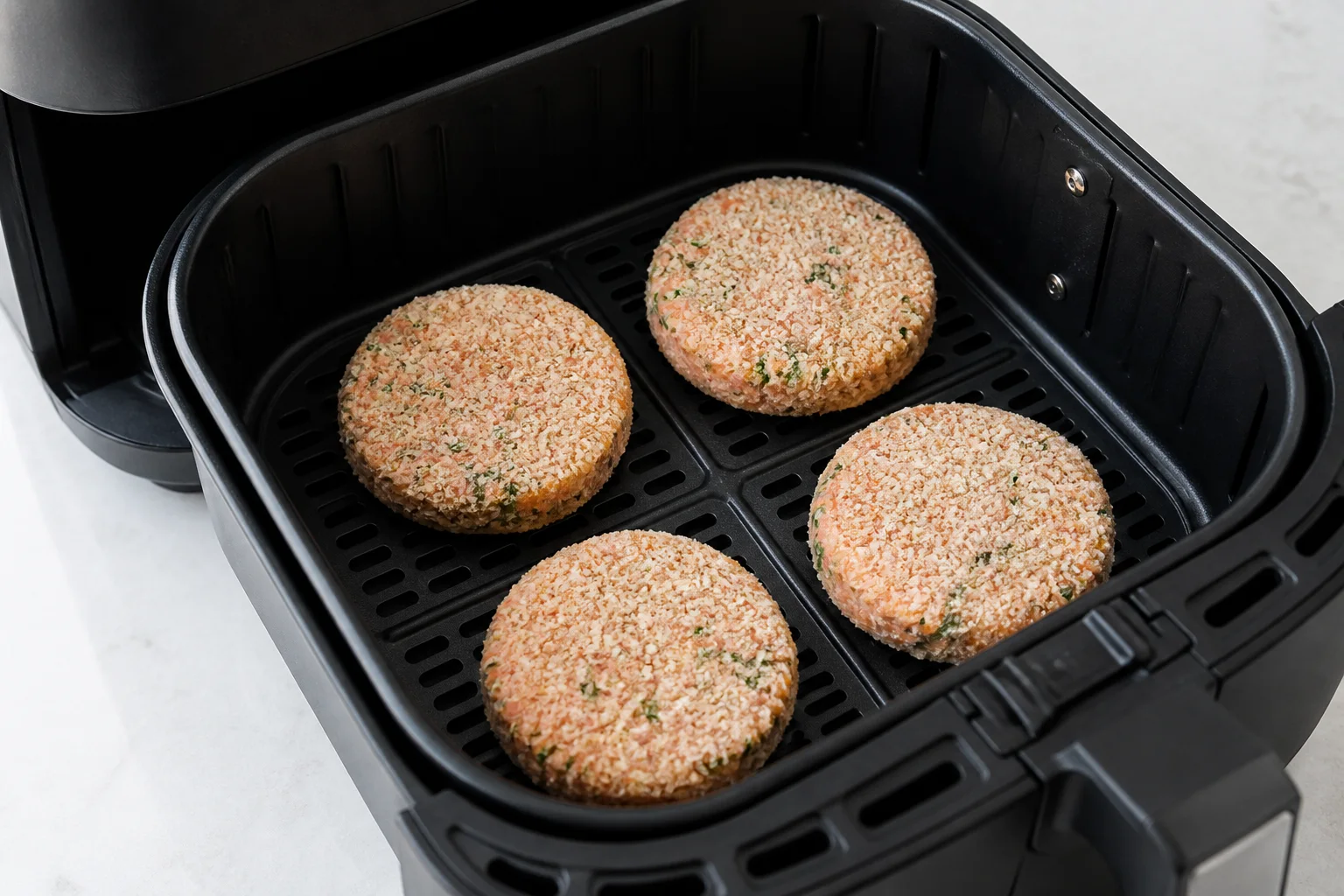 Four uncooked panko-coated salmon patties spaced in a single layer in an air fryer basket
