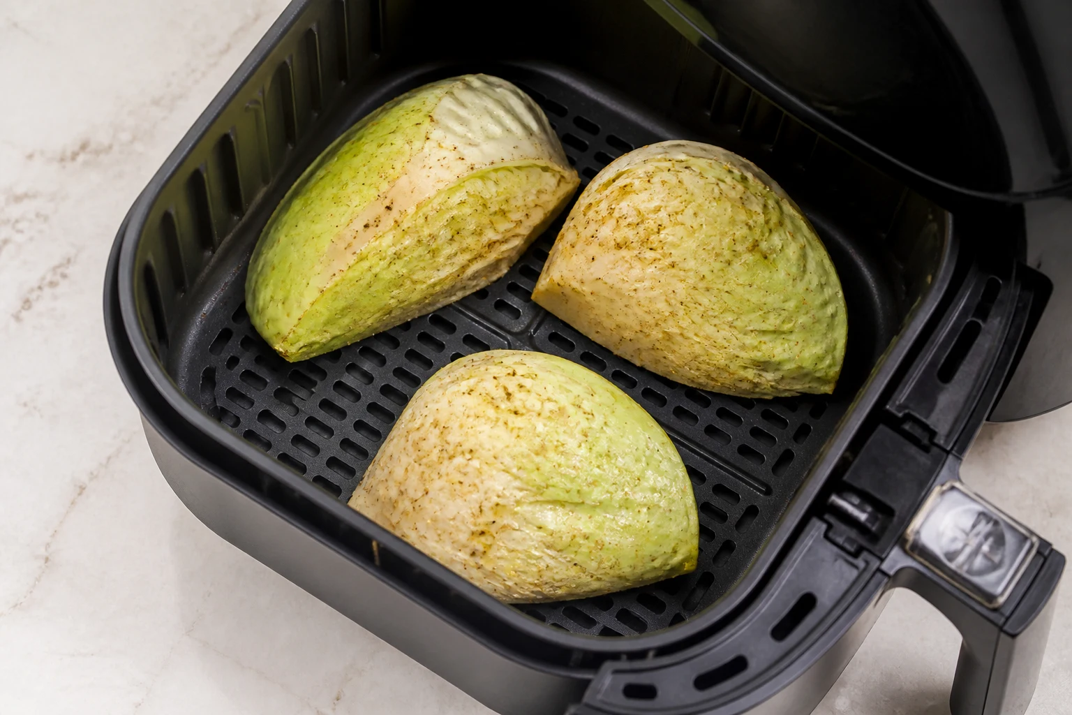 Compact seasoned cabbage wedges placed cut-side down in an air-fryer basket with ample space.