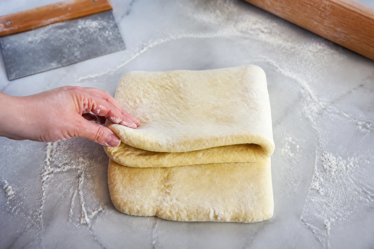 Layered cottage-cheese biscuit dough being folded into thirds on a lightly floured counter.