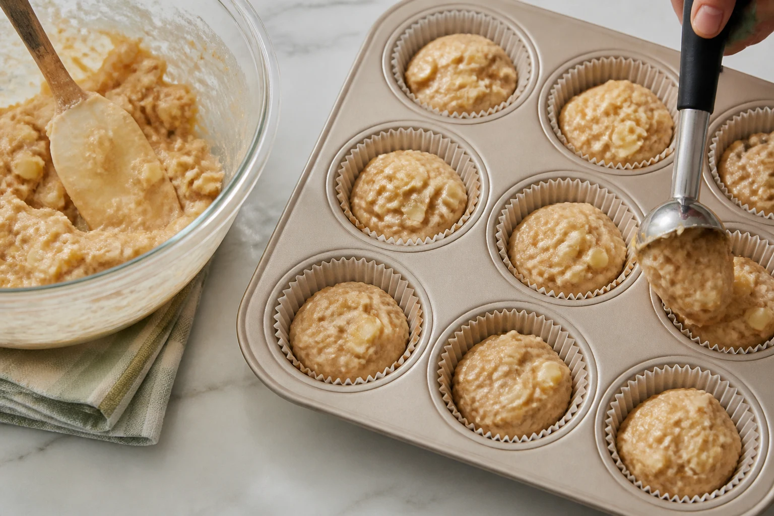 apple muffin batter being folded gently and portioned evenly into a lined 12-cup pan.