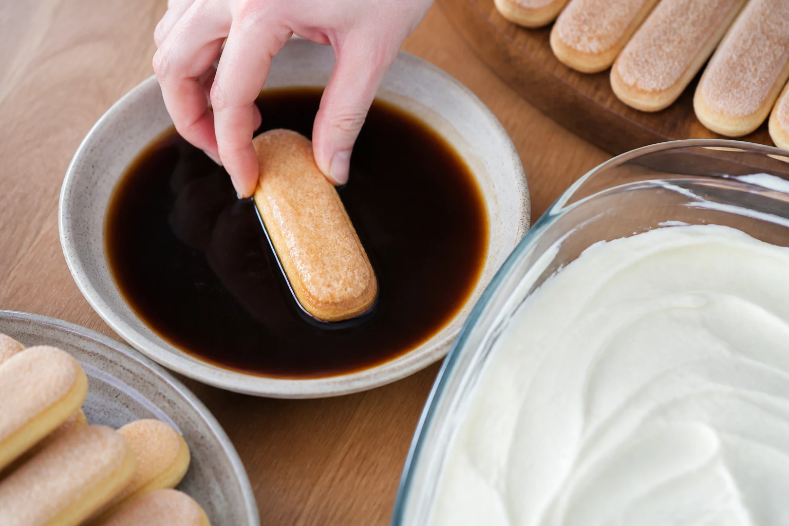 Ladyfingers being dipped quickly in cooled espresso before layering with thick yogurt-mascarpone cream.