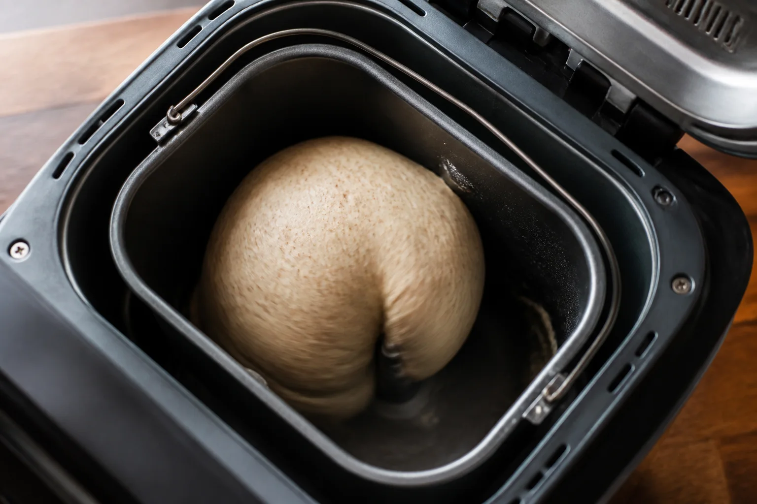 Soft cohesive high-fiber bread dough forming a tacky ball during kneading inside a bread-machine pan
