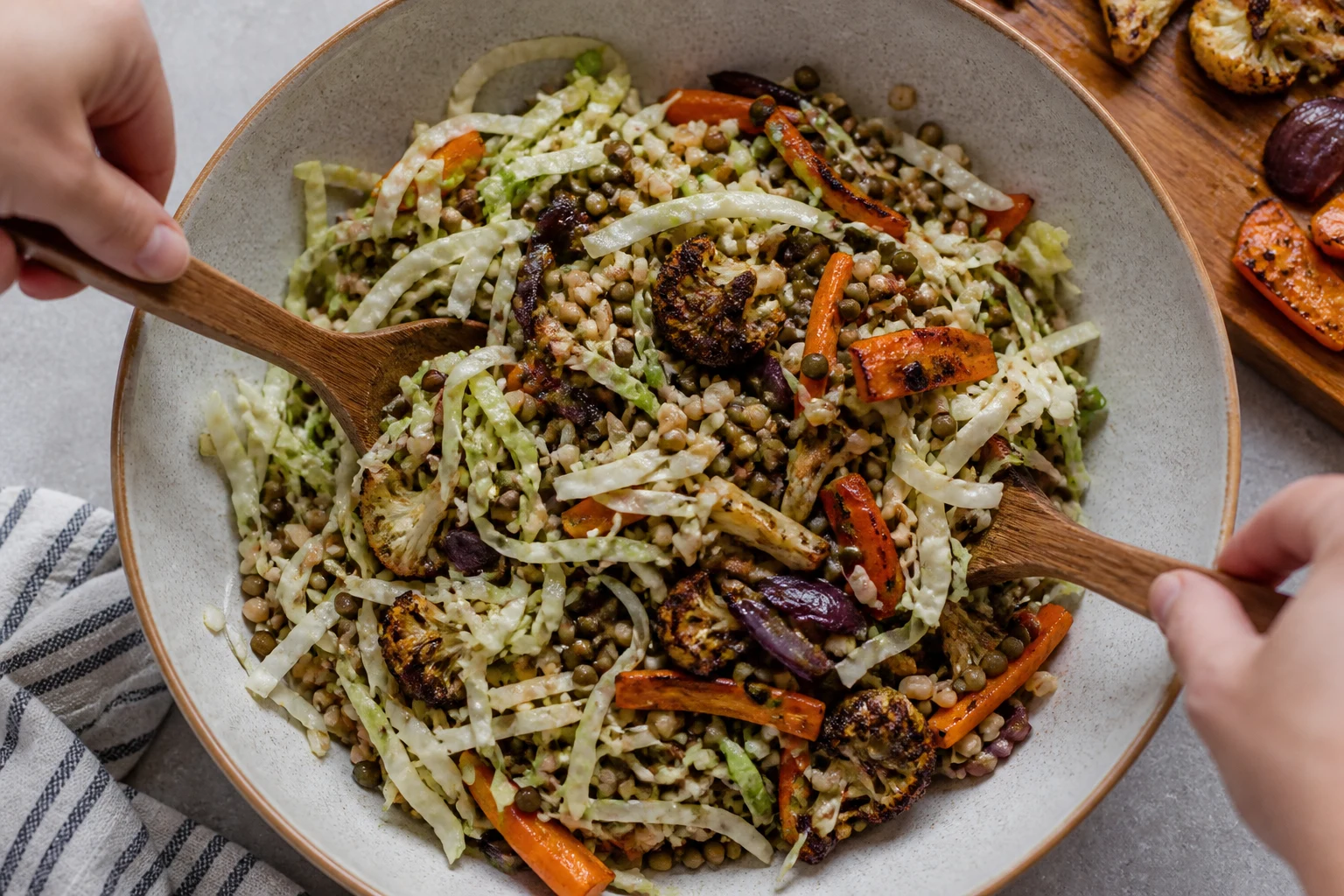 Cooled roasted vegetables being folded gently into dressed lentils, barley and finely shredded cabbage.