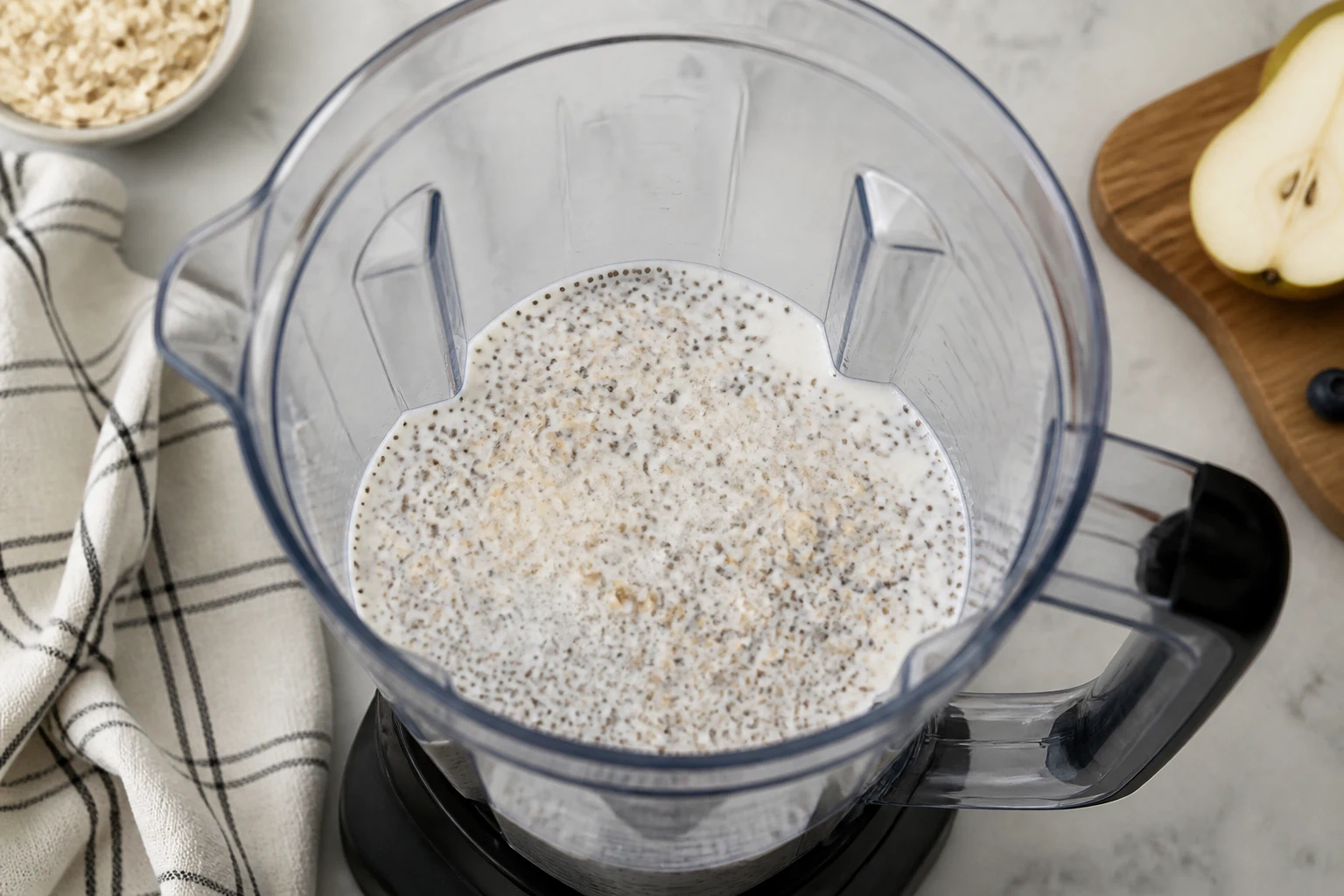 Oats and chia hydrating in milk inside a blender before pear, berries and yogurt are added.