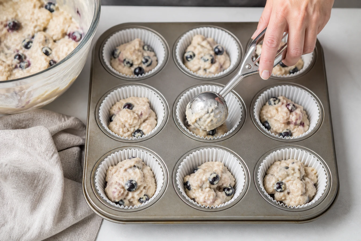 Blueberry-studded high-protein muffin batter being divided evenly among lined muffin cups.