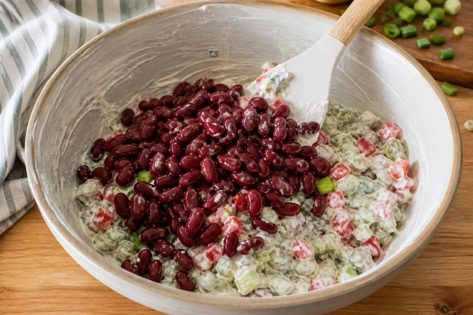 Dry red kidney beans being folded into creamy dressed celery, pepper, pickles and scallions with a broad spatula